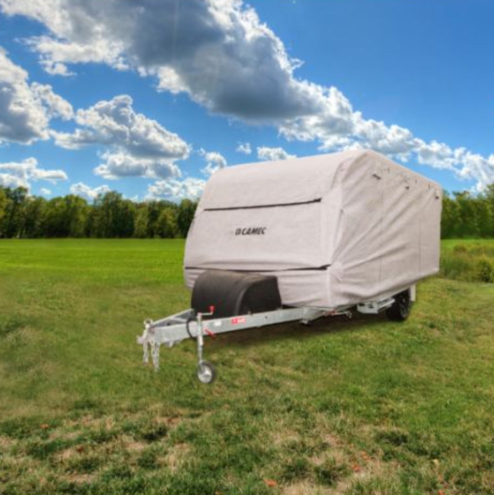 A beige RV cover placed on a caravan, situated in an outdoor setting with a clear sky and trees in the background.