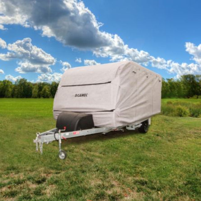 A beige RV cover placed on a caravan, situated in an outdoor setting with a clear sky and trees in the background.