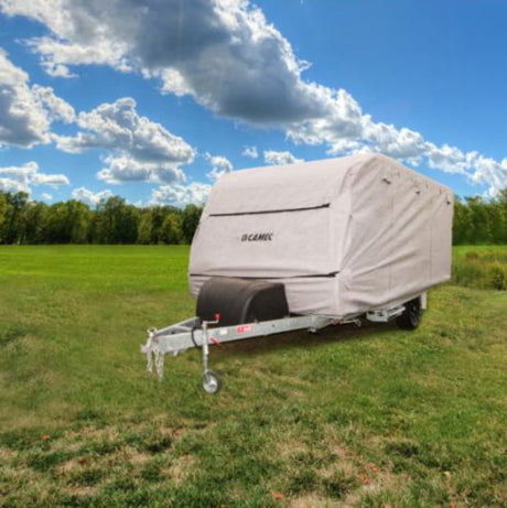 A beige RV cover placed on a caravan, situated in an outdoor setting with a clear sky and trees in the background.
