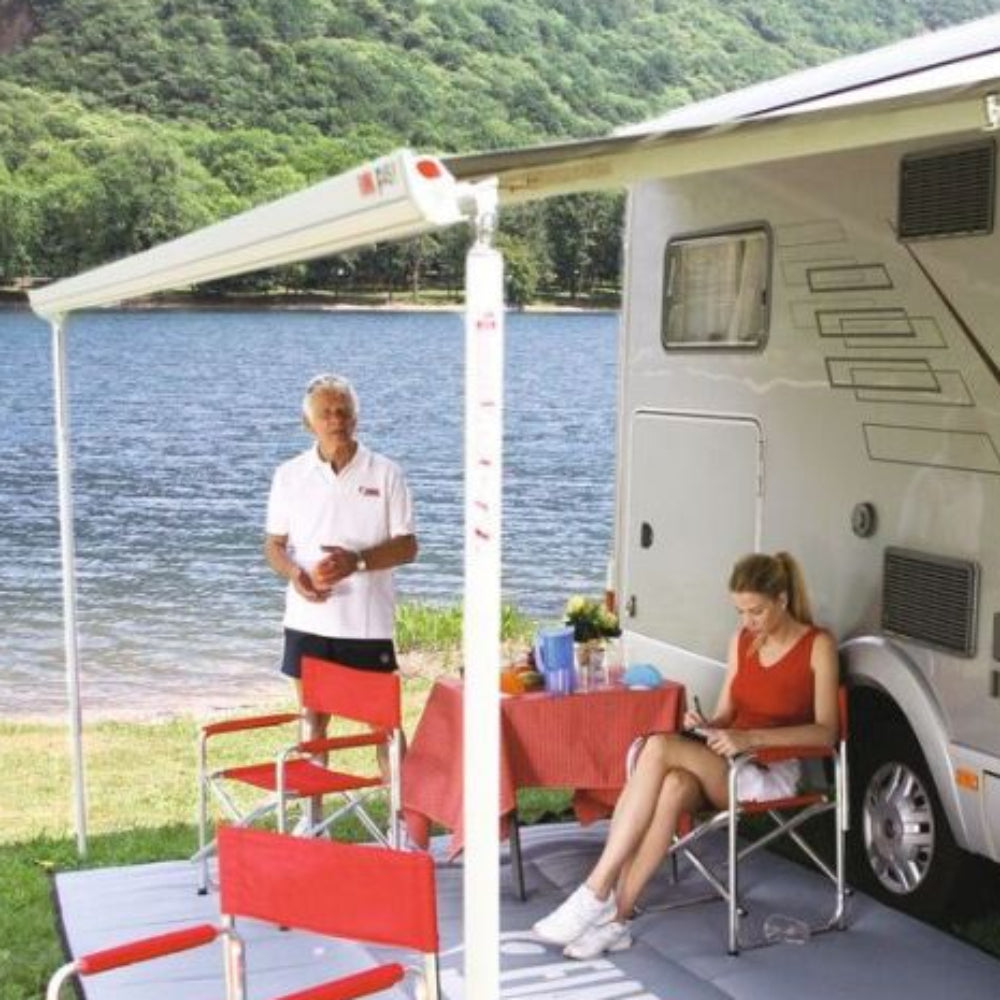 An awning set up beside a motorhome with a man standing and a woman sitting at a table on the awning's shade.