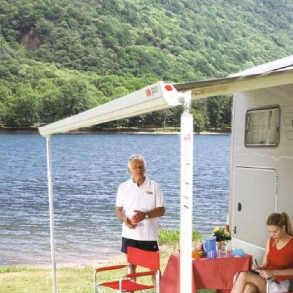 A man and a woman sitting under an extended motorhome awning by a lakeside