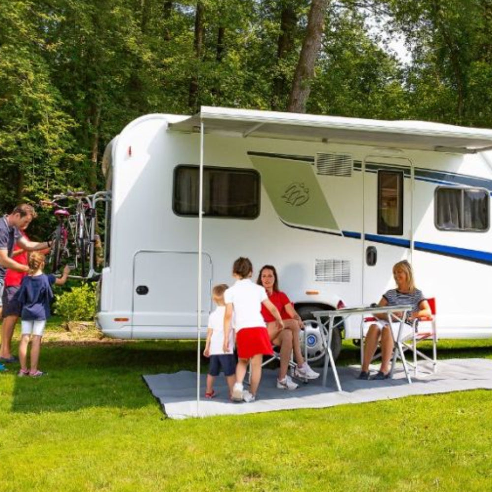 An extended Fiamma F45 S awning in white, attached to a campervan, providing shade for people seated at a small table underneath it.