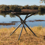 Metallic folding stool in a natural setting with water and trees in the background