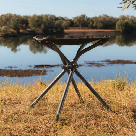 Metallic folding stool in a natural setting with water and trees in the background