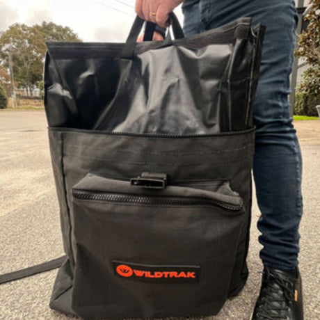 Person holding a black bag with a Wildtrak logo outdoors.