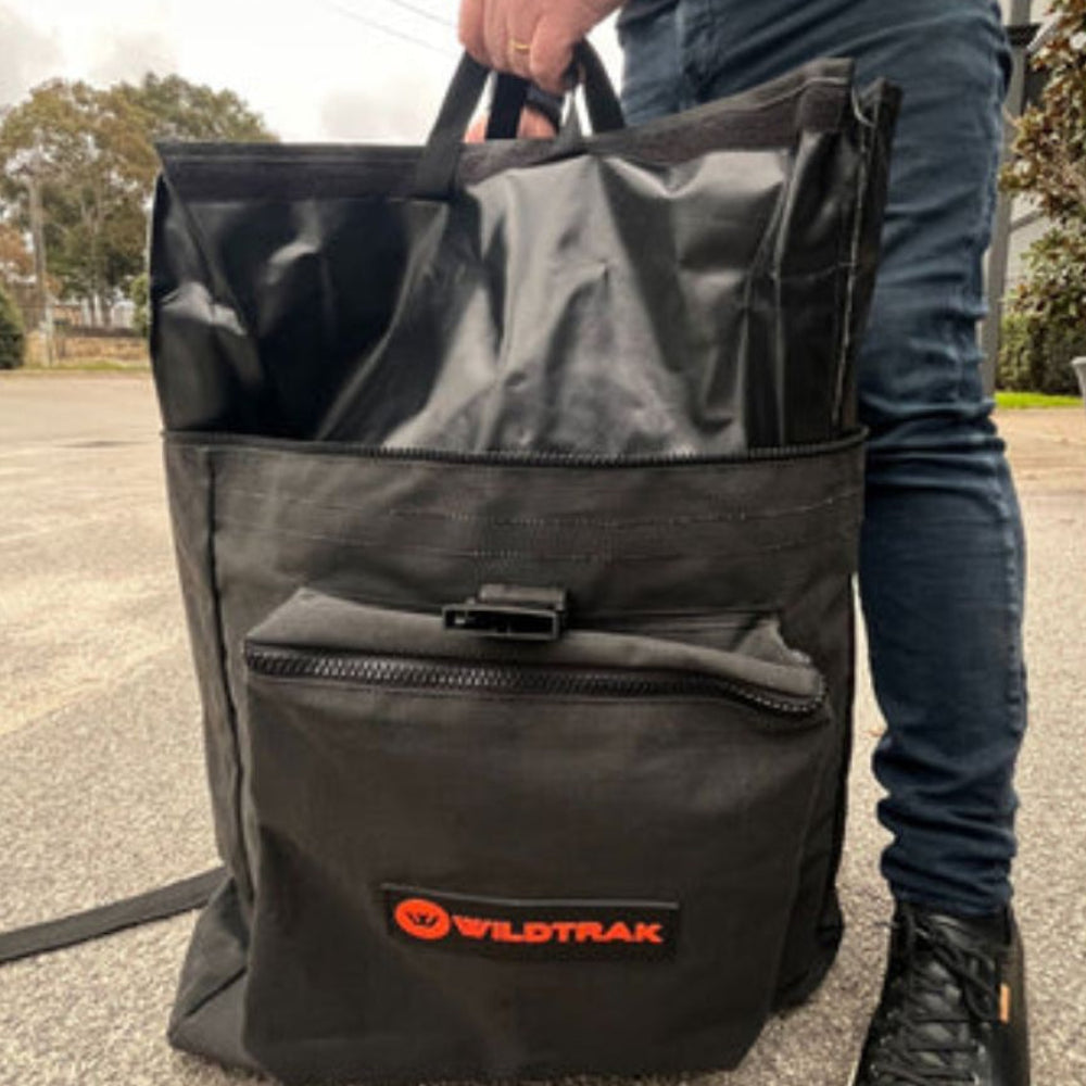 Person holding a black bag with a Wildtrak logo outdoors.