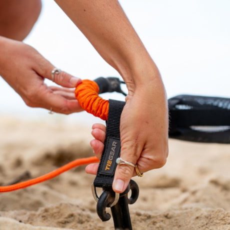 Person holding aTiegear Soft Spring with an orange handle on a beach