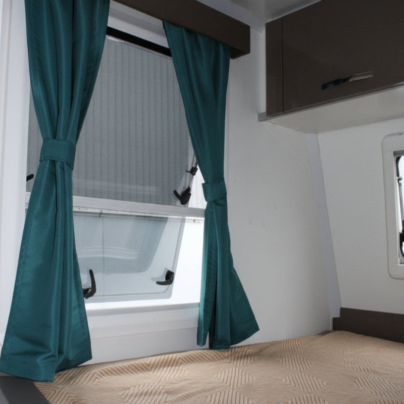A curtain tied back, revealing a window with a built-in blind, installed in a caravan interior.