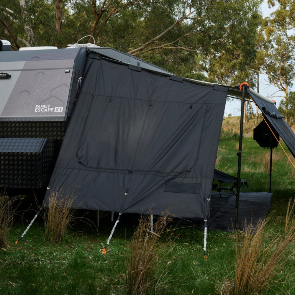 Black awning attached to a camper vehicle in a natural setting with trees and grass.