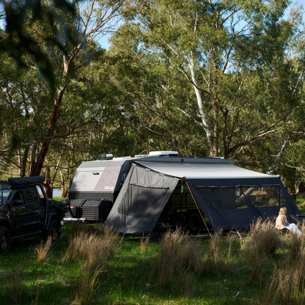 Camper van with a large awning set up in a forested area
